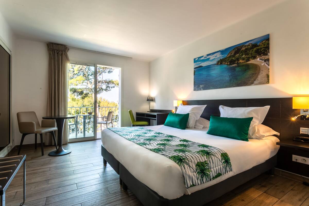 Habitación de hotel con una cama grande, un escritorio, una silla y un balcón con vistas al mar.