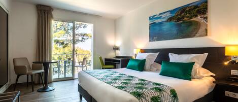 Habitación de hotel con una cama grande, un escritorio, una silla y un balcón con vistas al mar.