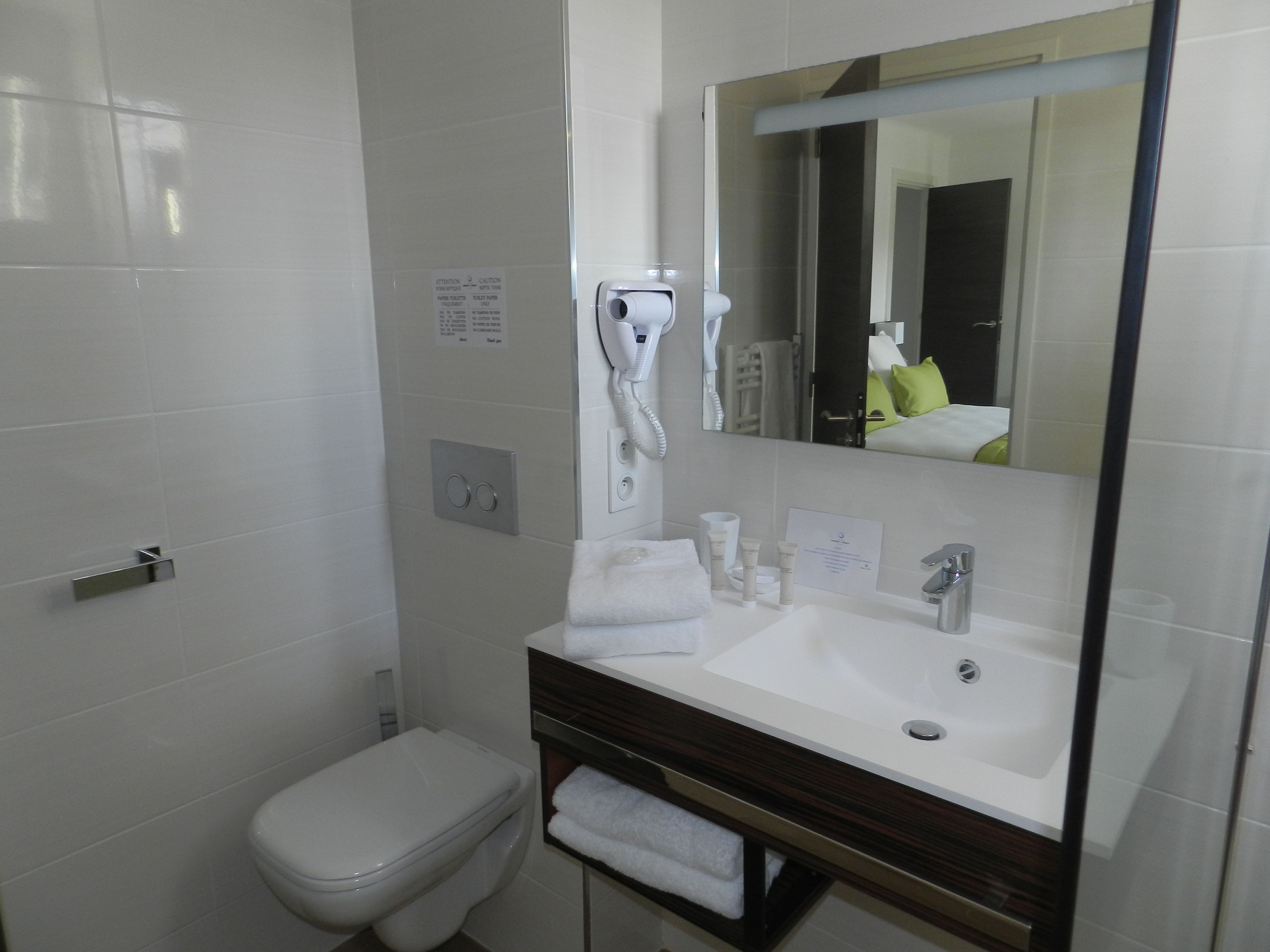 A modern bathroom with a white toilet, a sink with a mirror above it, and a hairdryer mounted on the wall.
