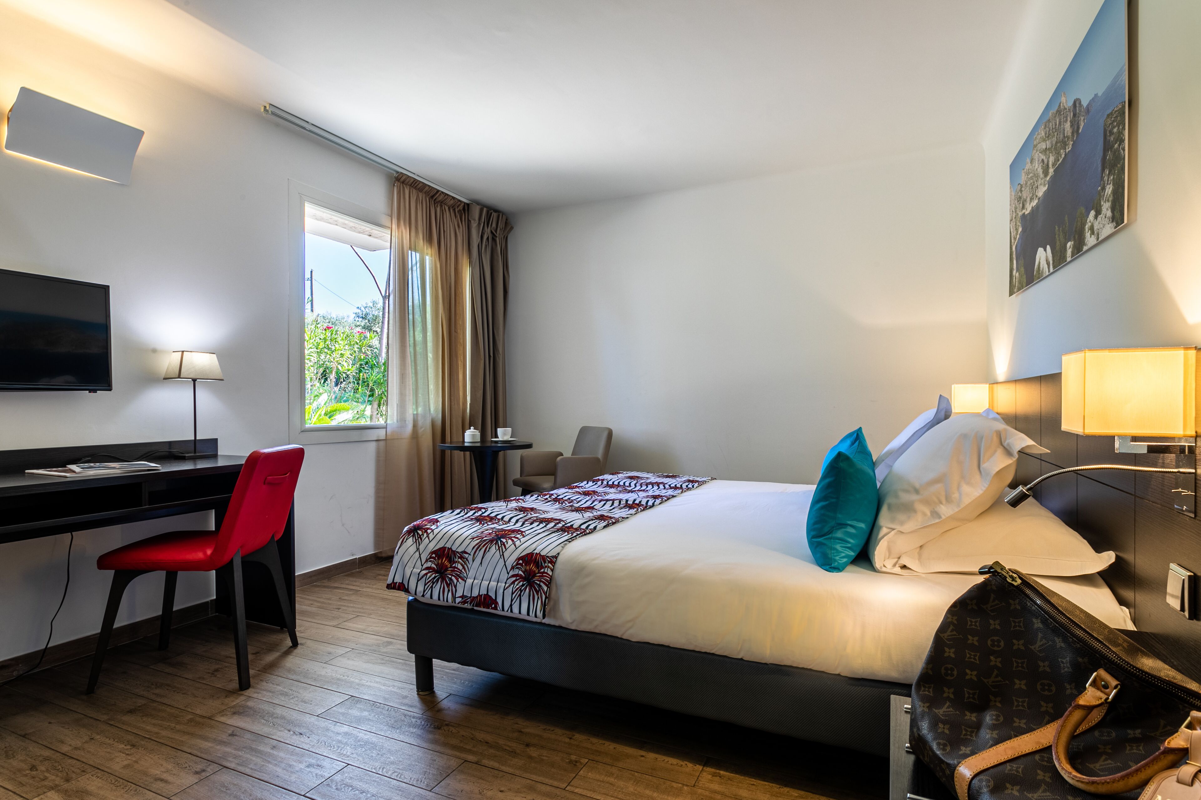 A hotel room with a bed, a desk, a chair, a TV, and a window with curtains.