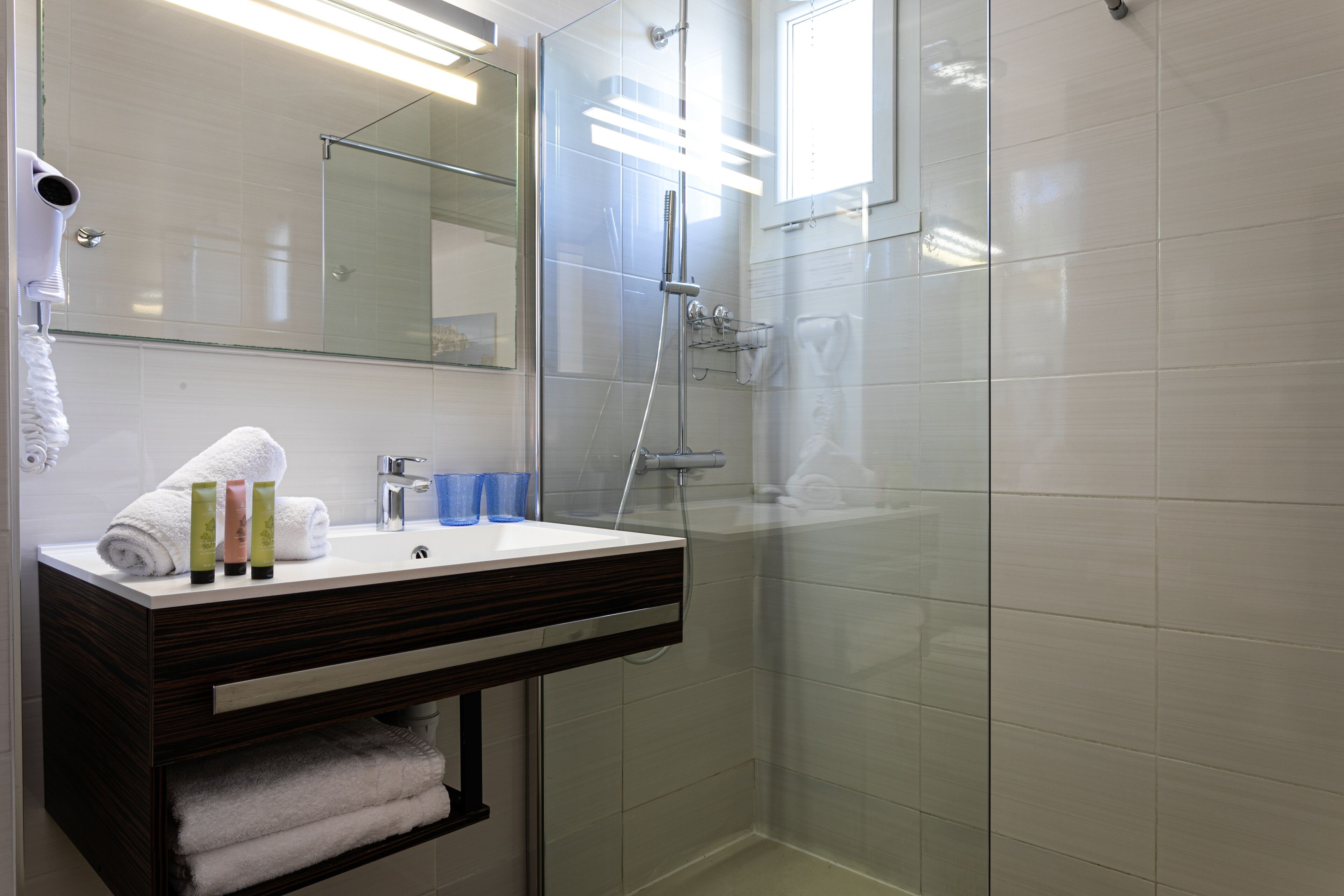 Un baño con ducha de vidrio, tocador con espejo y artículos de aseo.