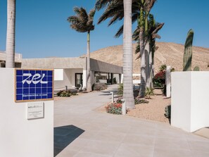 A hotel entrance with a blue sign, palm trees, and a desert landscape. - Zel Fuerteventura - Adults Only (Pajara)