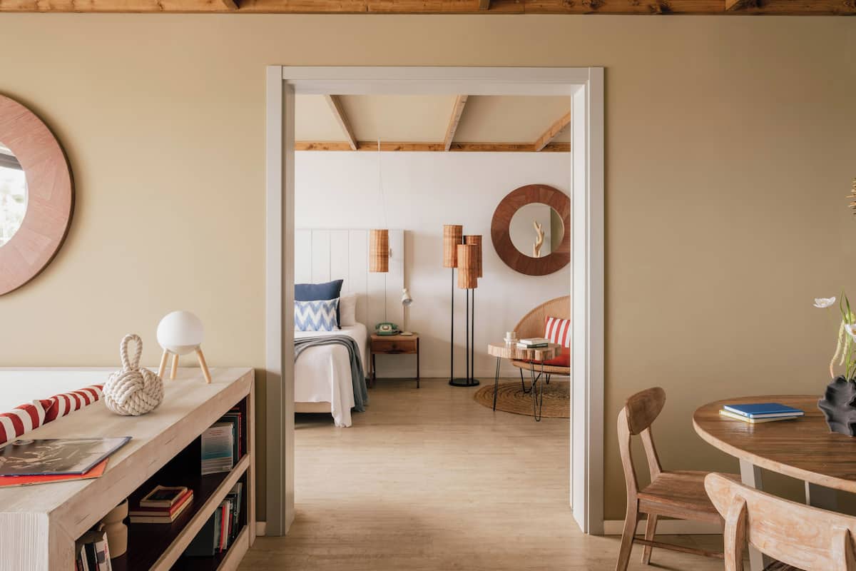 A room with a bed, bedside table, bookshelves, a round mirror, and a dining area with chairs and a table.