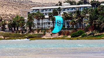 Ein Strandhotel mit Pool, Palmen und einer Person, die Kitesurfen geht.