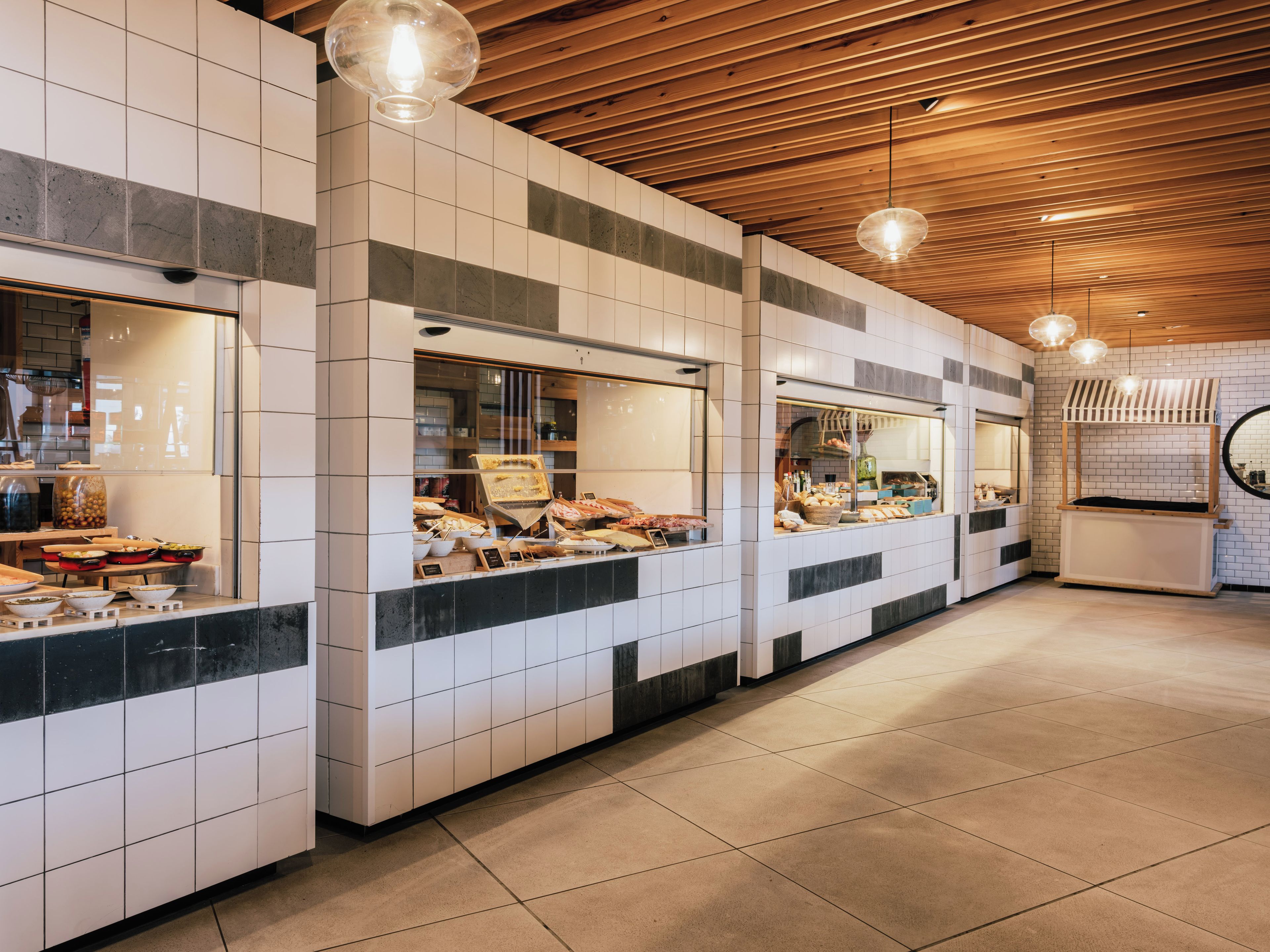 Un área de servicio de alimentos limpia y moderna con paredes de azulejos, techo de madera e iluminación colgante.