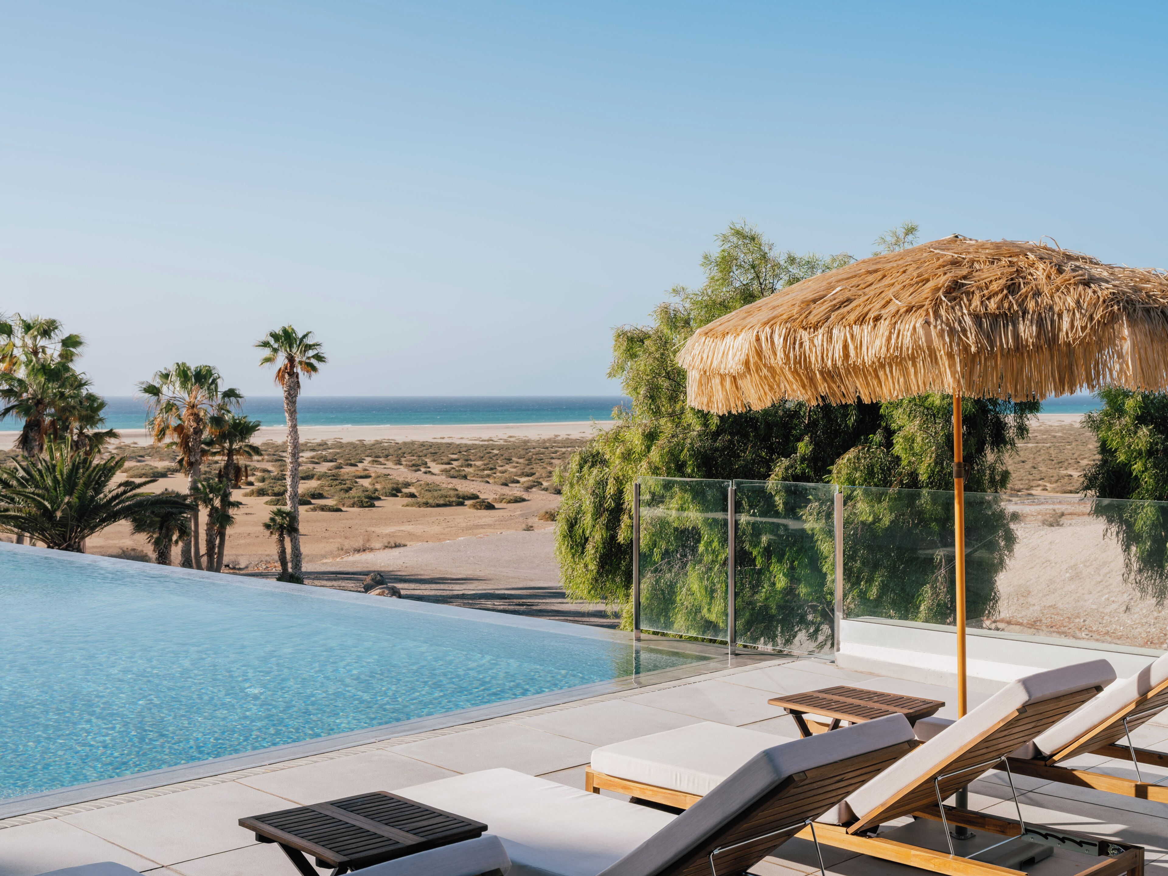 Una piscina al aire libre, sombrillas, sillones reclinables de piscina