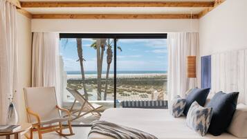 Une chambre avec un grand lit, un fauteuil à bascule, une vue sur la plage et un plafond en bois.