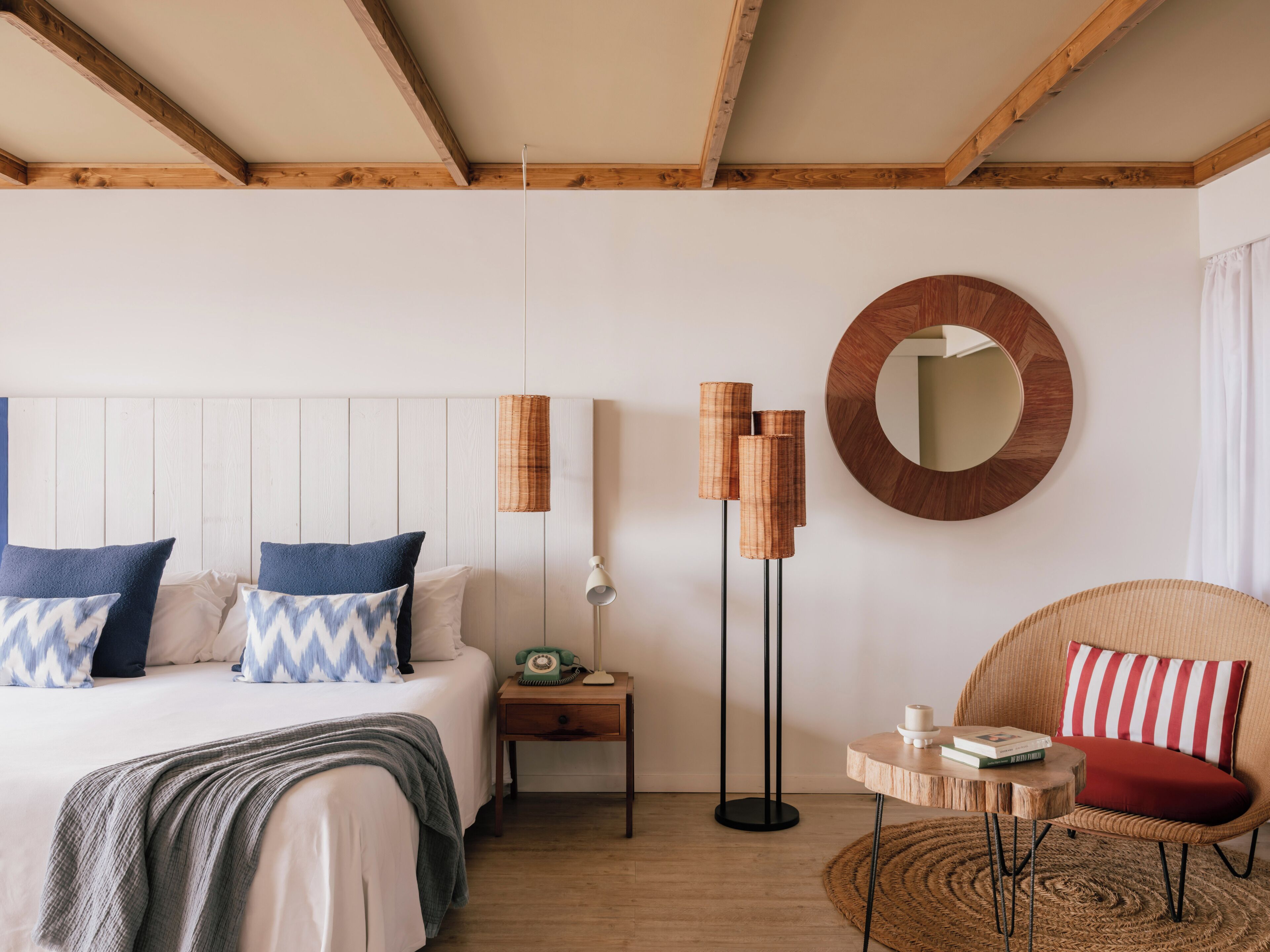 Une chambre à coucher avec un lit, une table de chevet, une lampe, une chaise et un miroir rond accroché au mur.