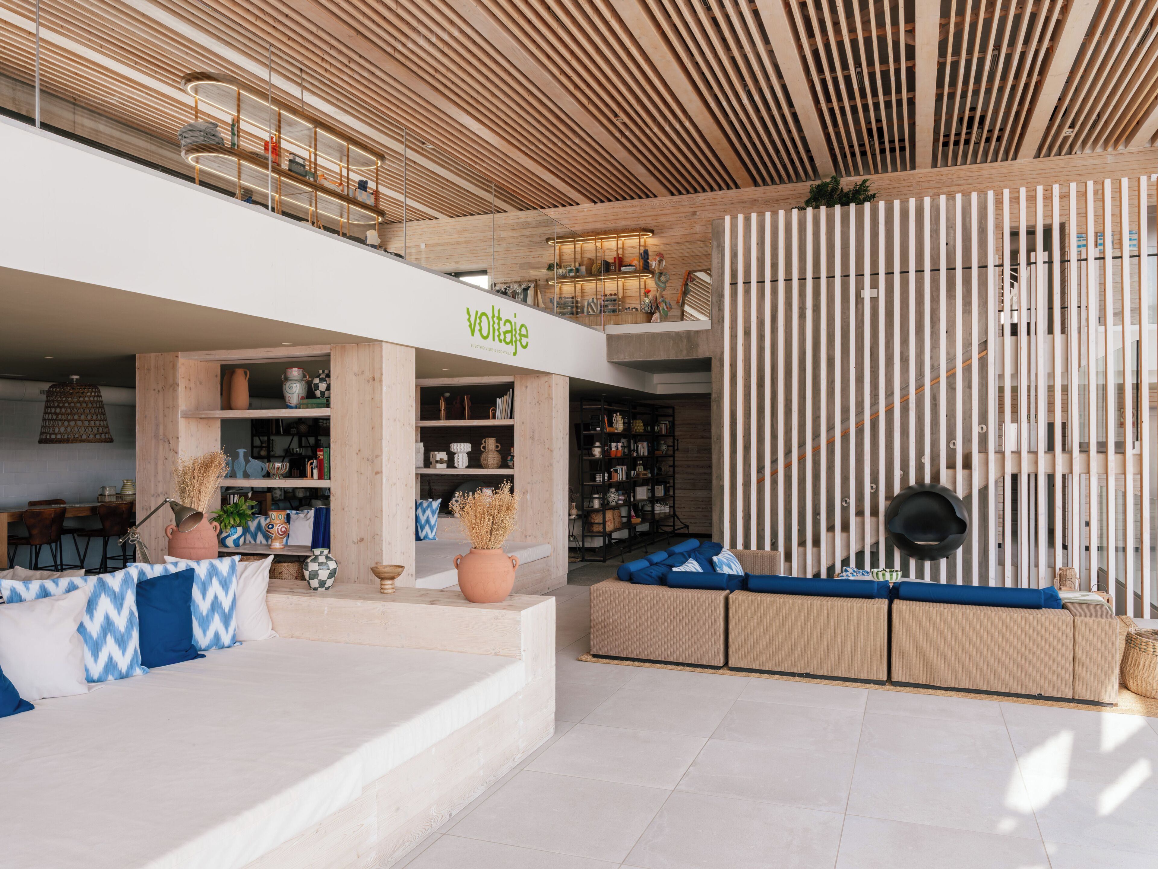 Een modern interieur met een houten plafond, een zithoek met blauwe kussens, en een 'voltajé' bord.