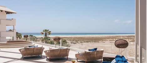A balcony with wicker furniture, a wooden table, and a view of the beach.