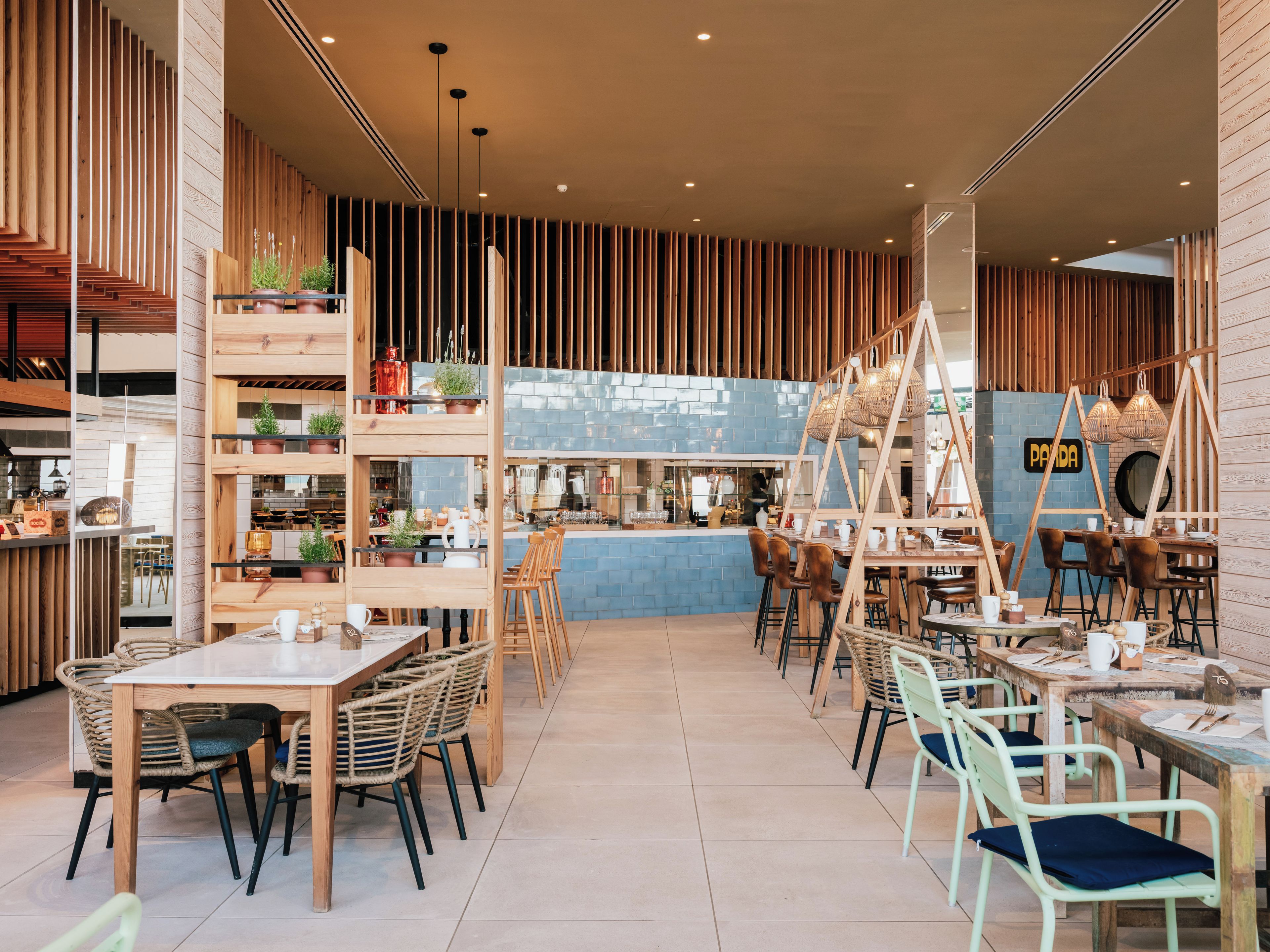 Een modern café interieur met houten details, een blauw betegelde toonbank en verschillende zithoeken.