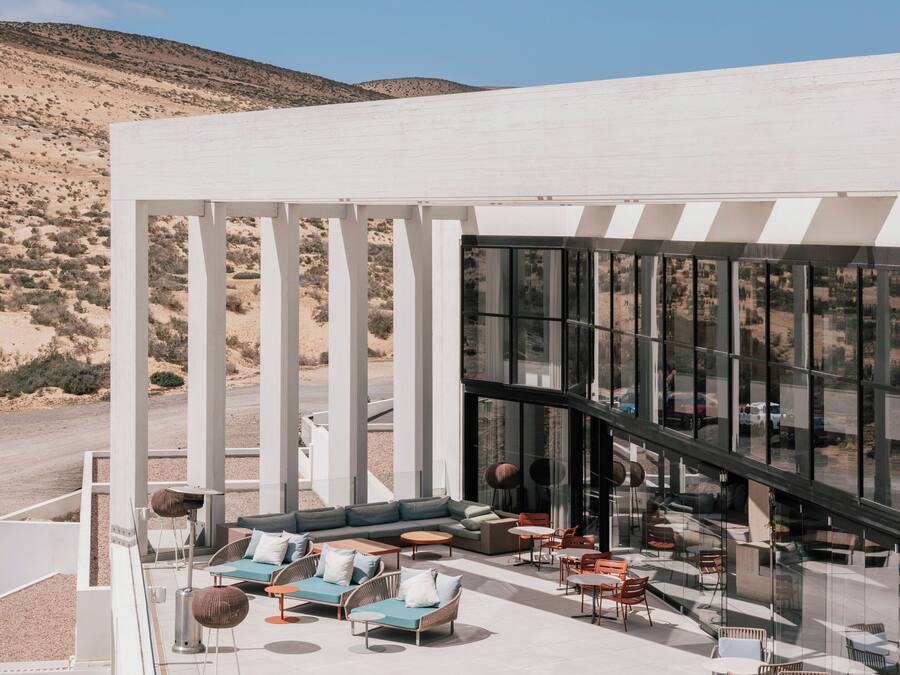 Un área de lounge exterior moderna con asientos y un espacio con paredes de vidrio.