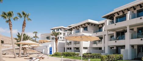 A modern hotel with multiple floors, outdoor seating with umbrellas, and palm trees.