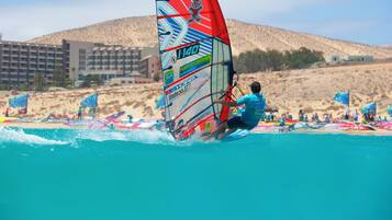 Una persona practica windsurf en una playa, con un edificio al fondo.