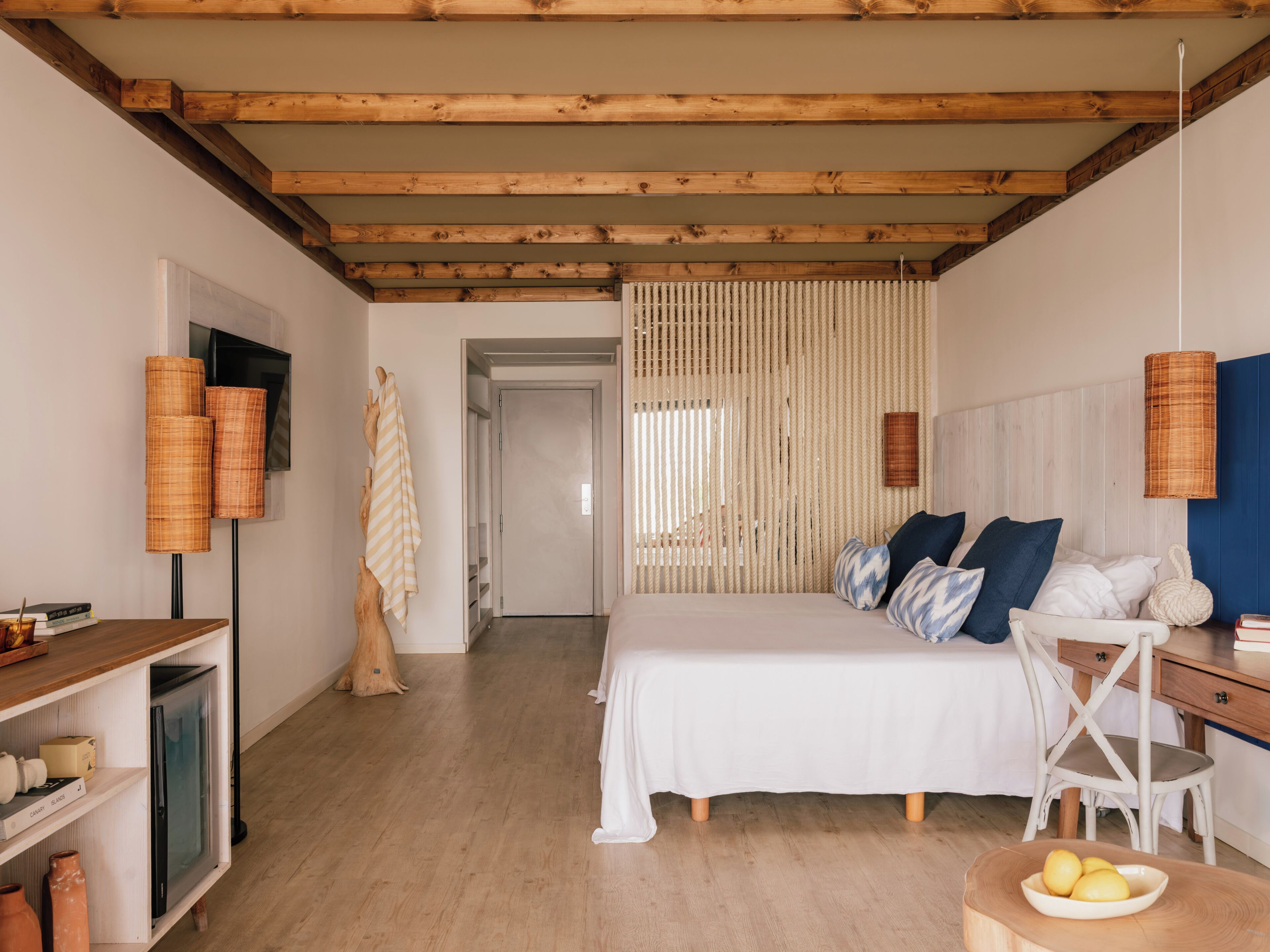 A bedroom with a bed, a desk, a chair, a television, and a door leading to another room.