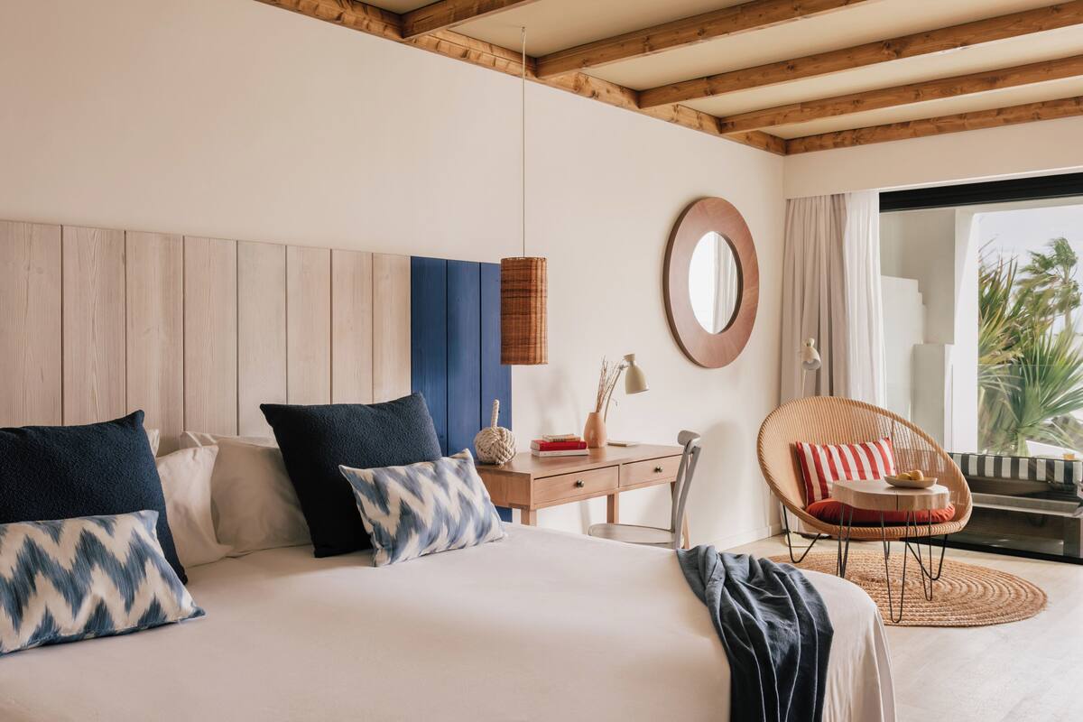 A bedroom with a bed, bedside table, chair, and a view of the outdoors.