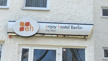 Letrero de un hostal con un logotipo y el nombre 'enjoy hostel Berlin City West'.
