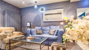Een moderne woonkamer met een glazen salontafel, een blauwe bank en een grote spiegel.