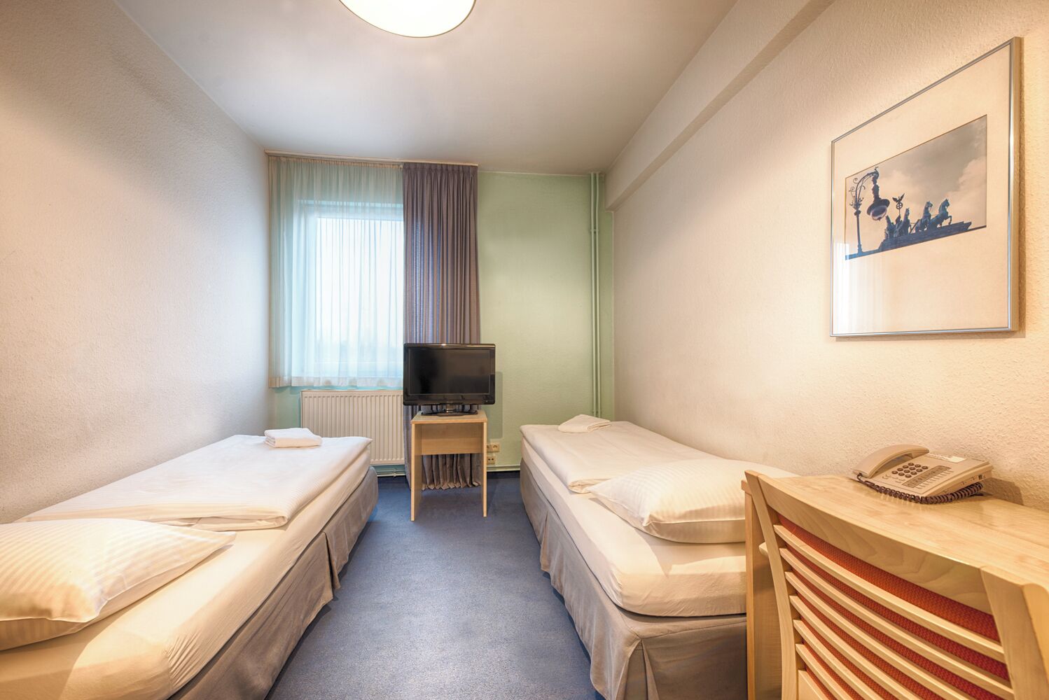 Een hotelkamer met twee eenpersoonsbedden, een kleintje tafeltje met een televisie, een telefoon en een ingelijst schilderij aan de muur.