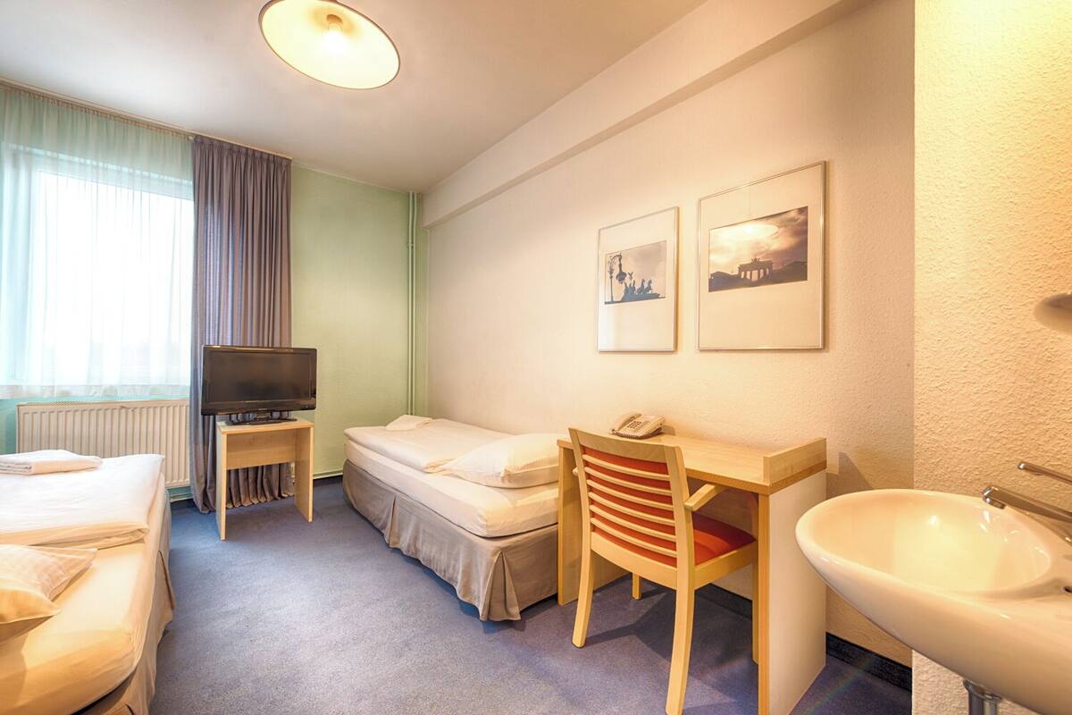Een hotelkamer met een bed, een bureau met stoel, een televisie en een wastafel.