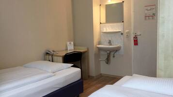 A hotel room with two beds, a desk with a telephone, a non-smoking sign, a sink, and a door with a fire safety sign.