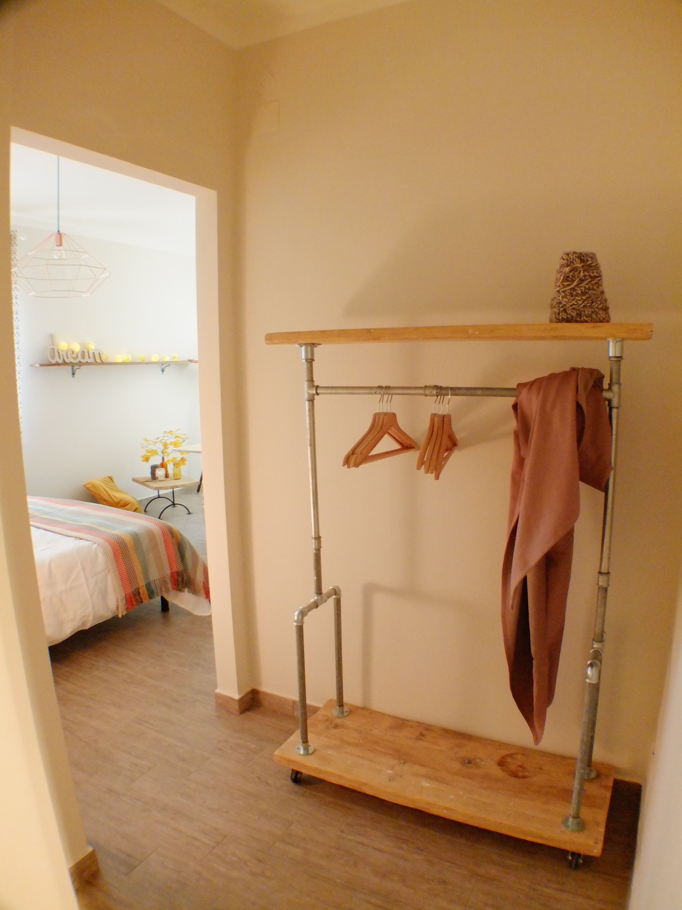 A room with a metal rack for hanging clothes, a bed with a striped blanket, and a small table with a vase of flowers.