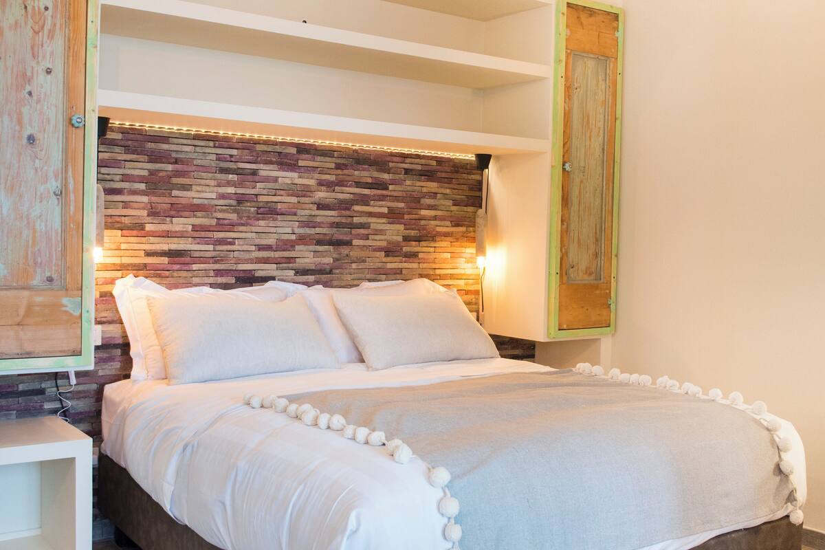 A bedroom with a wooden headboard, a bed with white bedding, and a bedside table.