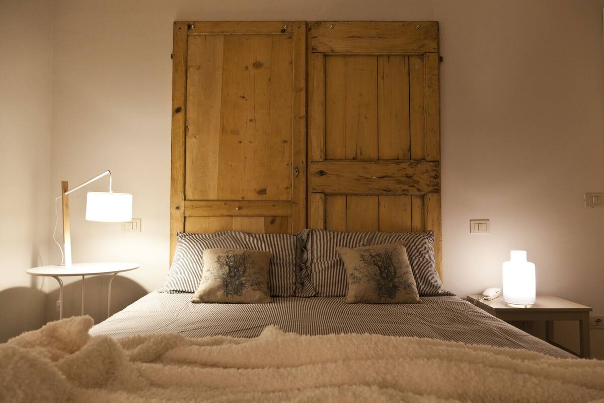 A bedroom with a wooden headboard, a bedside table with a lamp, and a bedside table with a white bottle.