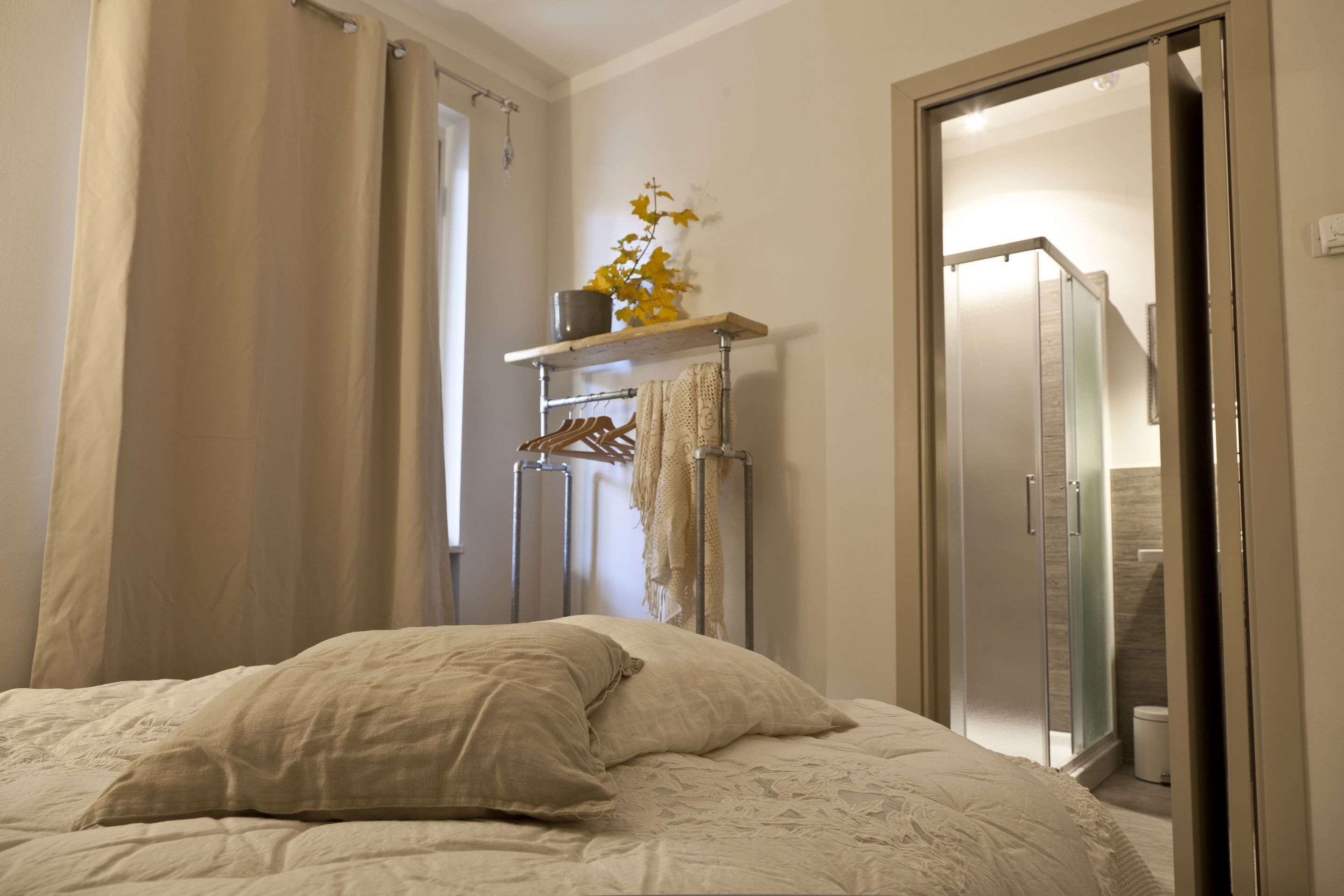 Un dormitorio con cama, armario, estante con una planta, y un baño visible a través de una puerta abierta.