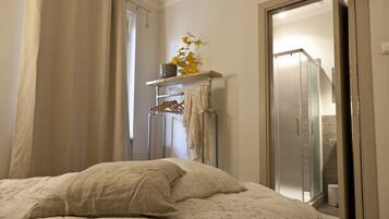 Un dormitorio con cama, armario, estante con una planta, y un baño visible a través de una puerta abierta.