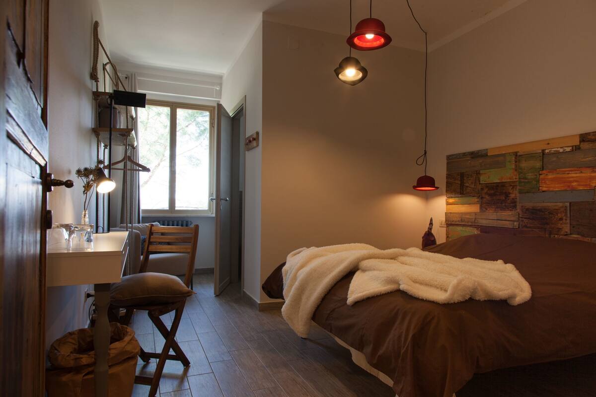 A bedroom with a bed, a desk with a chair, and a window.