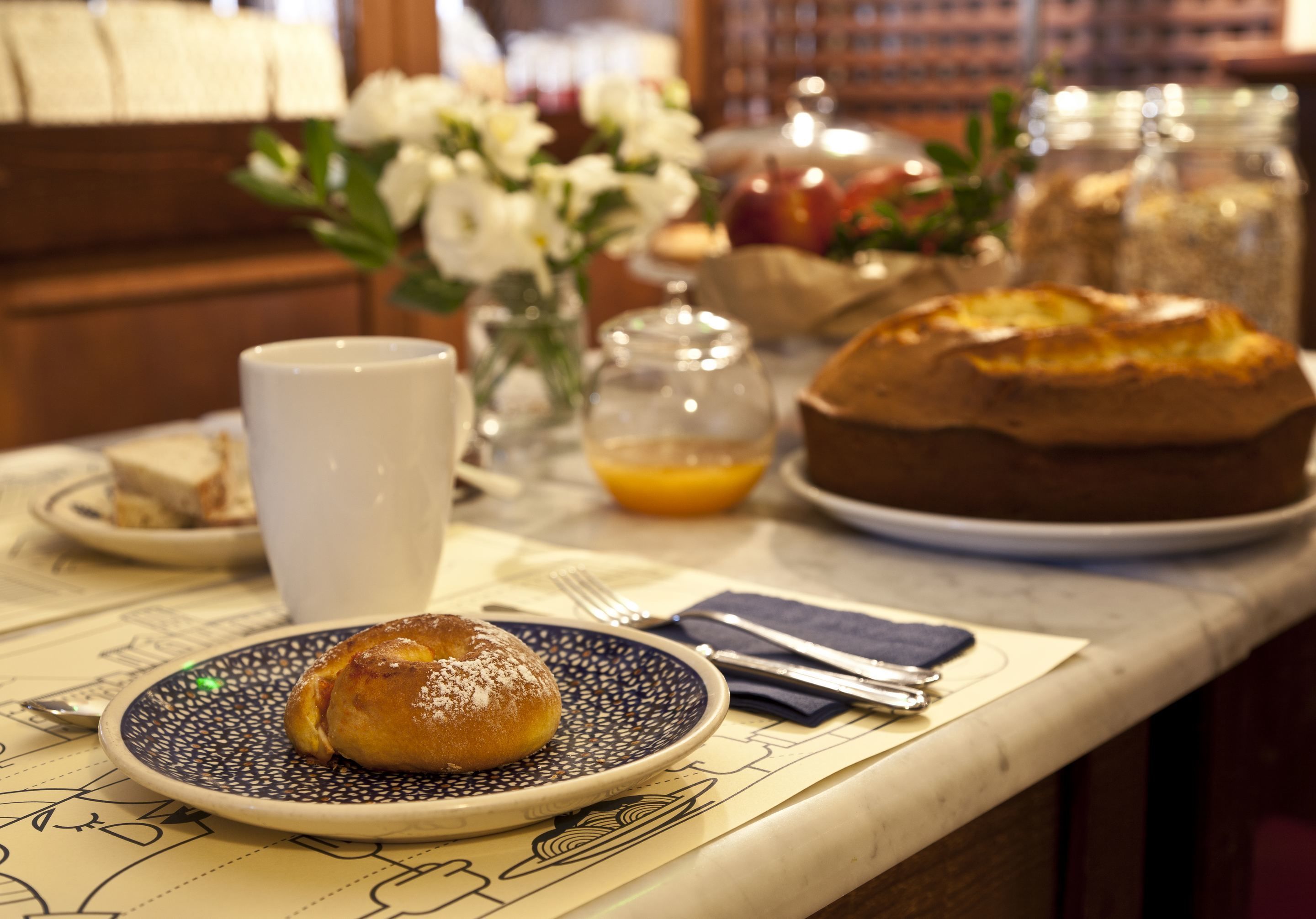 Une table mise pour le petit-déjeuner, avec une assiette de viennoiseries, une tasse et un vase de fleurs.