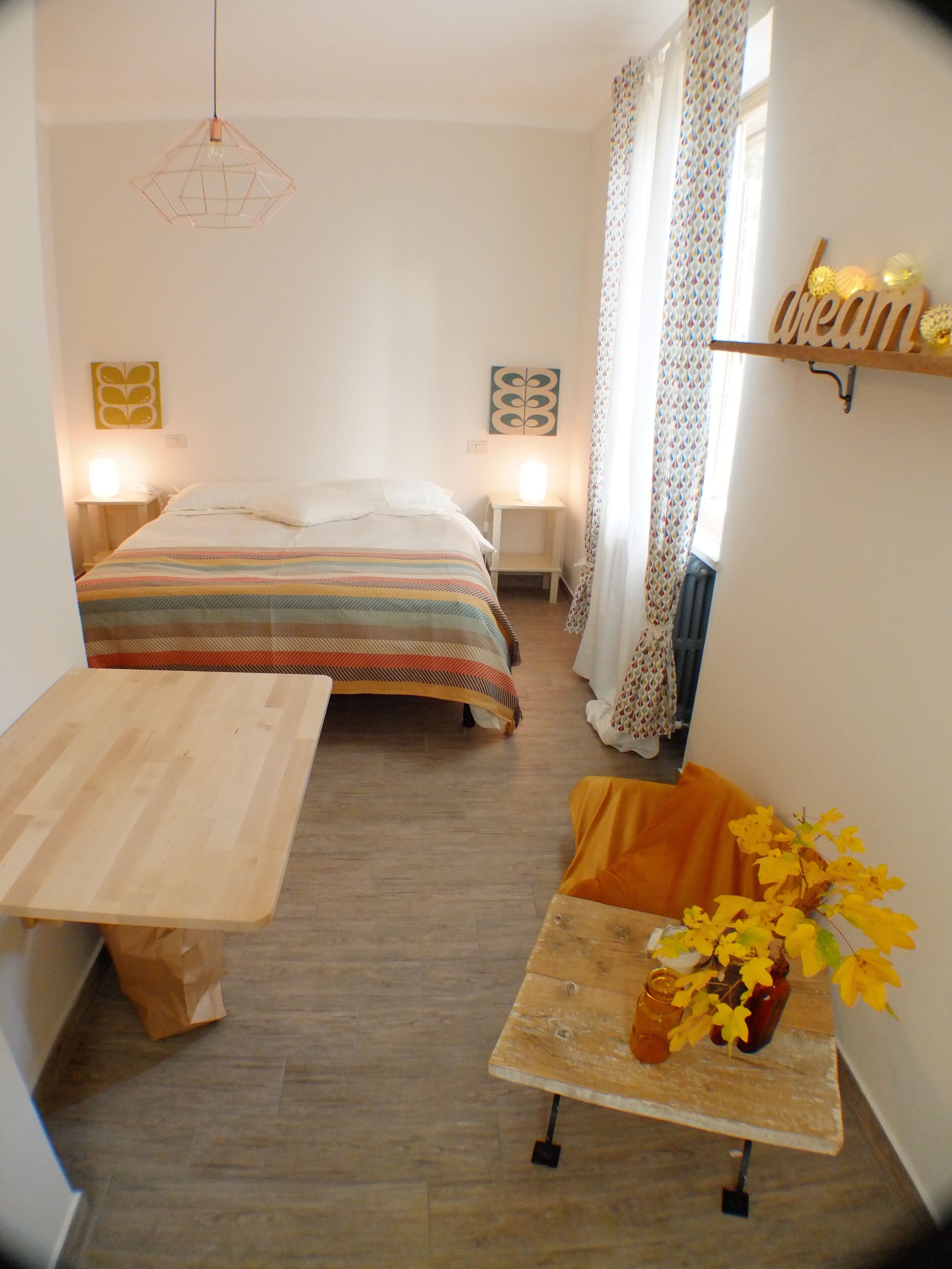 Ein kleines, gemütliches Schlafzimmer mit einem Bett, Nachttischen, einem Holztisch und einem kleinen Regal mit Dekoration.