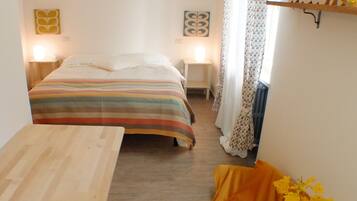 Ein kleines, gemütliches Schlafzimmer mit einem Bett, Nachttischen, einem Holztisch und einem kleinen Regal mit Dekoration.