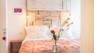 Un dormitorio con una cabecera de madera rústica, una colcha estampada en rosa y un florero con flores sobre una mesita de noche.