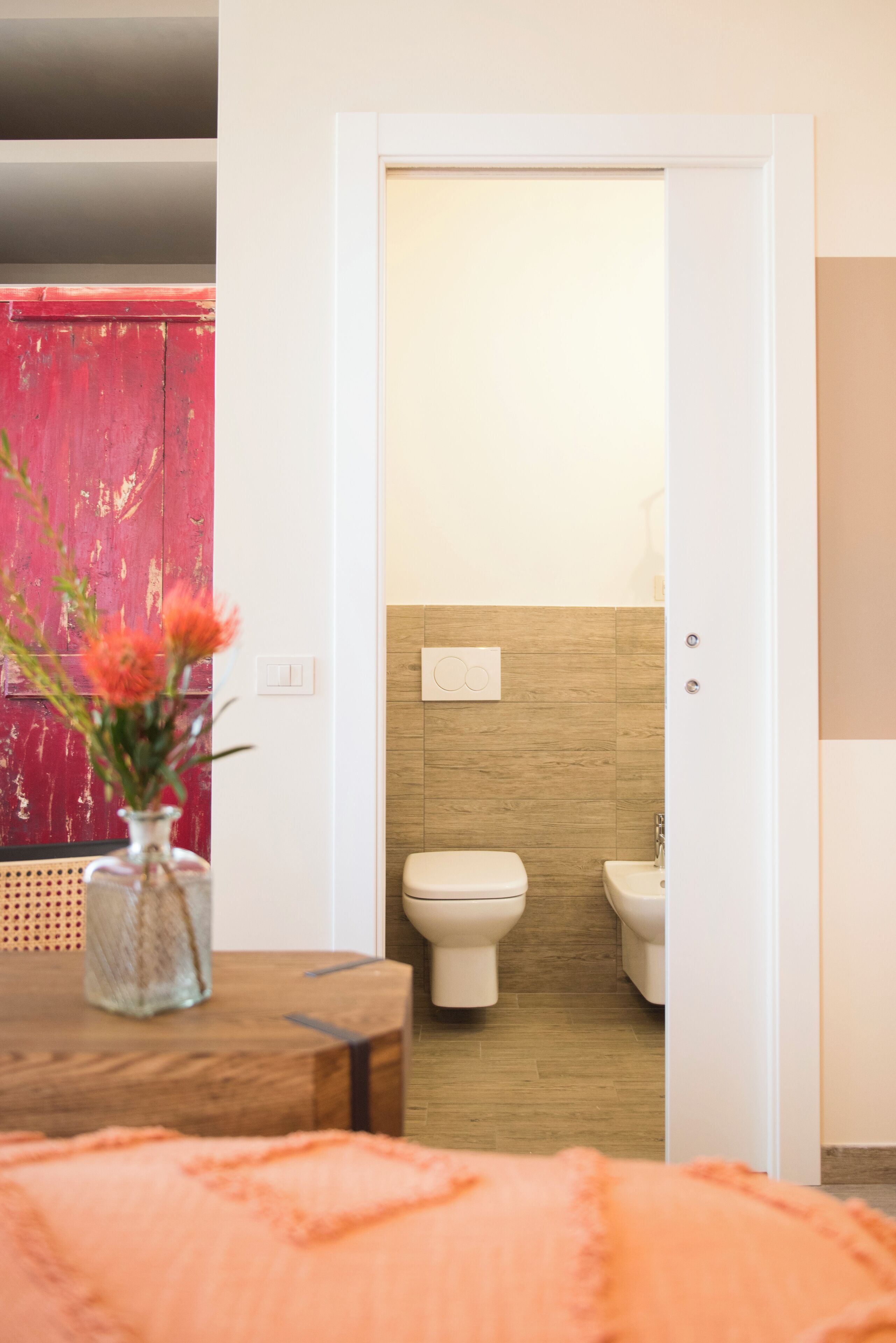 A modern bathroom with a toilet and bidet, a wooden floor, and a red door.