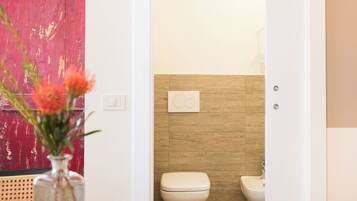 A modern bathroom with a toilet and bidet, a wooden floor, and a red door.