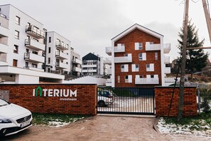 Ein verschlossener Eingang zu einem Wohnkomplex mit mehreren Mehrfamilienhäusern, einer Backsteinmauer mit dem Schriftzug "INTERIUM investment" und einem geparkten Auto davor.