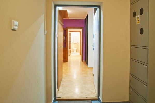 Käytävällä on puulattia, ja se johtaa huoneeseen, jonka seinät ovat violetit ja jossa on näkyvissä wc.