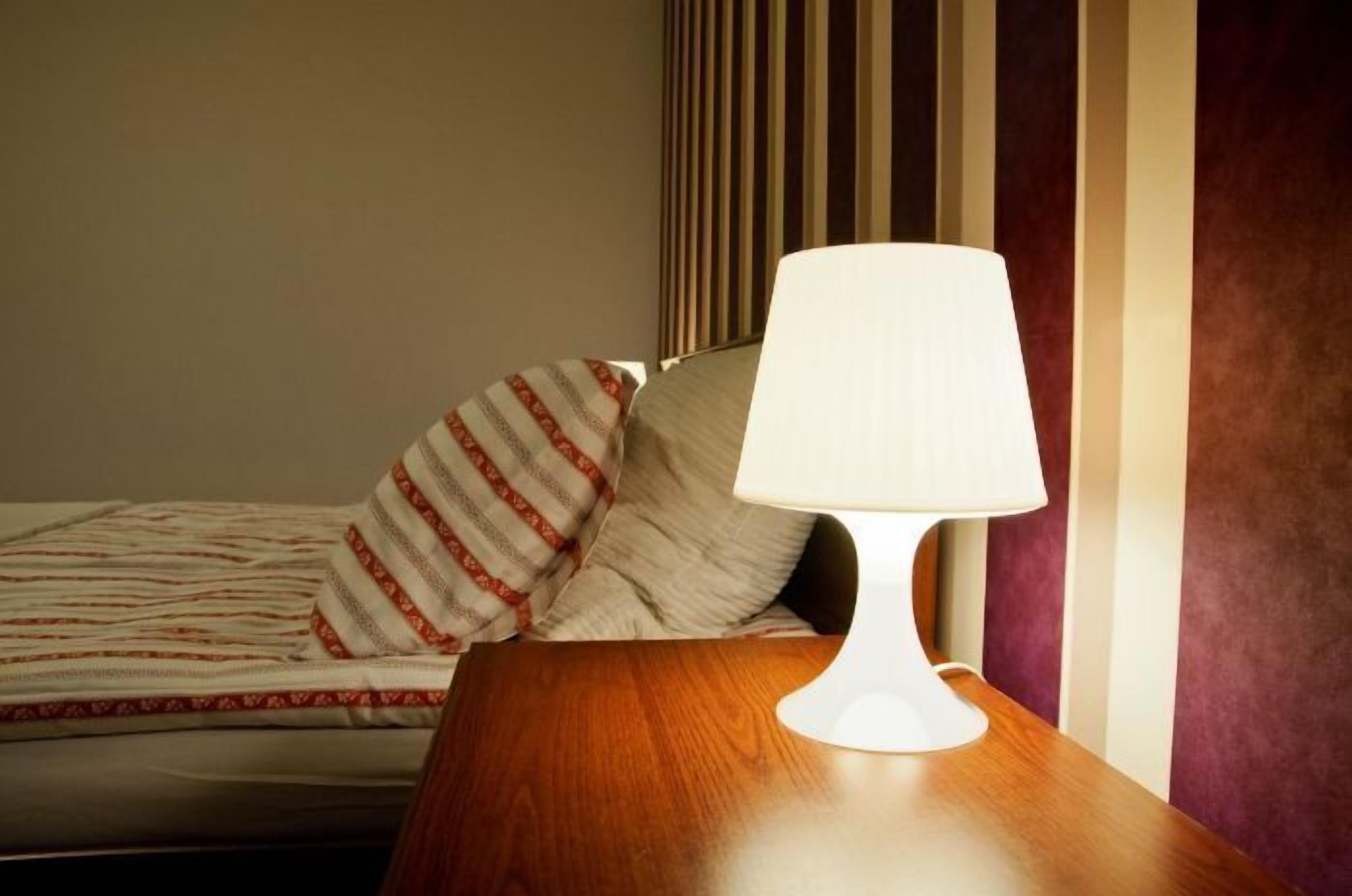 A hotel room with a bed, striped pillows, a wooden nightstand, and a white lamp.