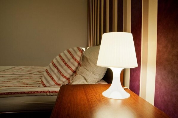 A hotel room with a bed, striped pillows, a wooden nightstand, and a white lamp.
