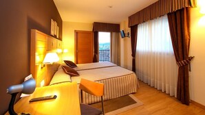 Habitación de hotel con cama, escritorio con lámpara, una silla y vistas al exterior a través de la ventana.
