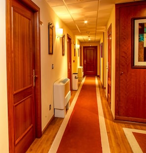 Un pasillo de hotel con puertas de madera, alfombra roja y un equipo de aire acondicionado blanco.