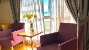 Una habitación con sillones morados, una pequeña mesa de madera y un florero con flores amarillas.
