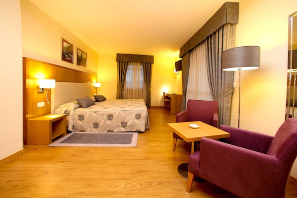 A hotel room with a bed, a desk, a chair, and a lamp.