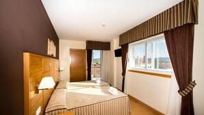 Habitación de hotel con una cama grande, cabecera de madera, escritorio y vista a la ciudad desde la ventana.