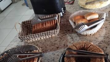 A kitchen counter with various food items and utensils, including a toaster, a bowl of bread, and a plate of sliced fruit.