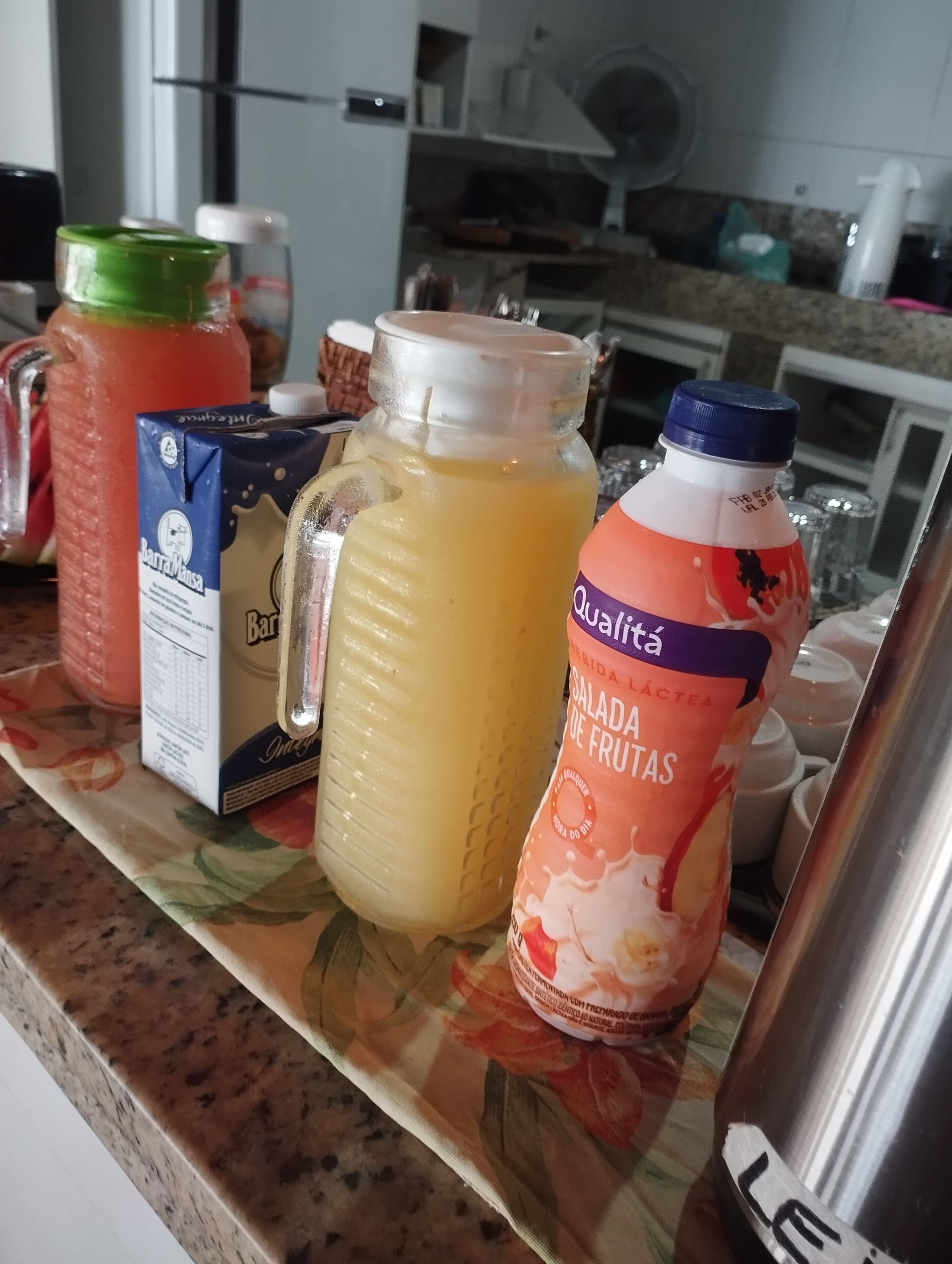 A kitchen counter with various food and drink items, including a carton of milk, a jar of sauce, and a bottle of fruit juice.