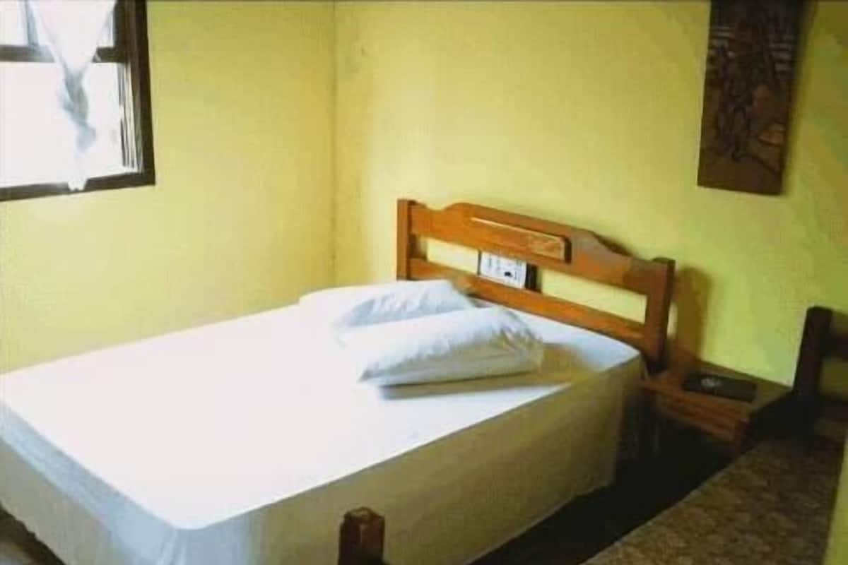 Una cama individual con cabecera de madera en una habitación con paredes amarillas y piso estampado.
