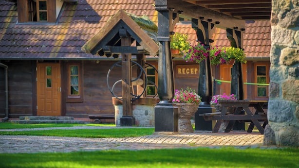 Un bâtiment rustique en bois, comprenant un espace d’accueil, un banc en bois et des paniers de fleurs suspendus.